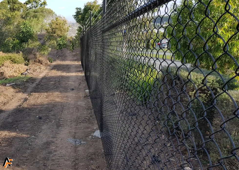 Industrial chain wire fencing installed along a service access track beside vegetation.
