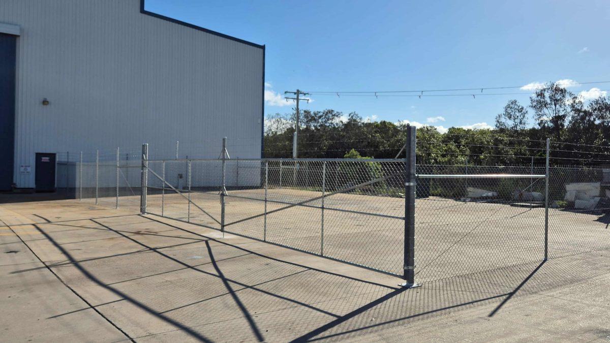 A galvanised chain wire security fencing section installed to separate a commercial yard, topped with barbed wire for added security. Installed by Apollo Fencing